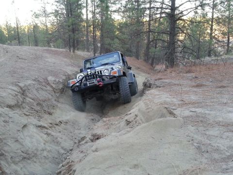 2005 Jeep Wrangler - A silver 2005 Jeep Wrangler navigates a steep, sandy off-road path surrounded by trees.