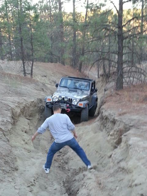 2005 Jeep Wrangler - A man walks down a steep dirt path as a silver 2005 Jeep Wrangler drives up the incline behind him.