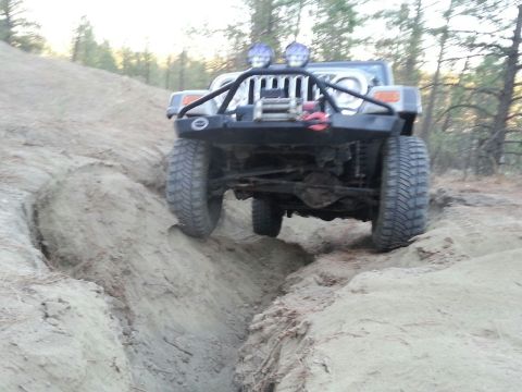 2005 Jeep Wrangler - A Jeep Wrangler navigates a challenging off-road trail, with its front tires deep in a sandy trench.