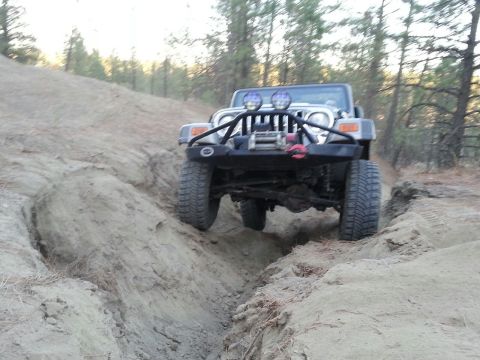 2005 Jeep Wrangler - A silver Jeep Wrangler navigates a challenging off-road trail with steep dirt banks.