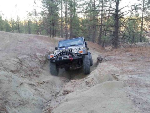 2005 Jeep Wrangler - A 2005 Jeep Wrangler tackles a challenging off-road trail, kicking up dust as it descends a steep incline.