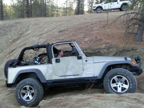 2005 Jeep Wrangler - A Jeep Wrangler Rubicon navigates an off-road trail, with a white pickup truck visible on the higher ground.