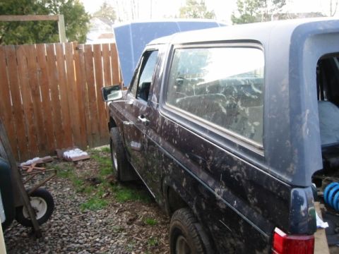 1985 Ford Bronco - This dark SUV, likely from the 1980s, is parked outdoors with its hood open.