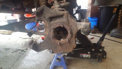 1983 Ford Bronco - A heavily corroded suspension component is supported by automotive repair equipment in a garage setting.