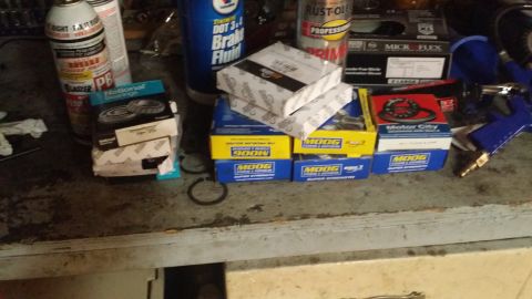 1983 Ford Bronco - Assorted automotive parts including bearings, brake fluid, and spray cans are laid out on a workbench.