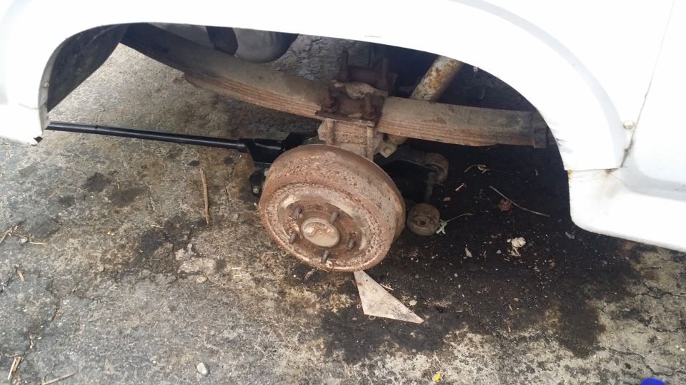 White vehicle's rusty rear drum brake and leaf spring suspension, jacked up