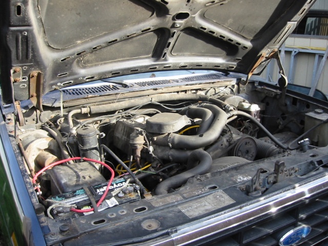 1985 Ford Bronco engine bay with V8 engine, battery, and hoses visible