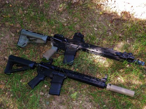 1996 Ford Bronco - Two assault rifles are lying on the grass. One rifle has a green stock and tan grip, while the other has a black stock and grip.