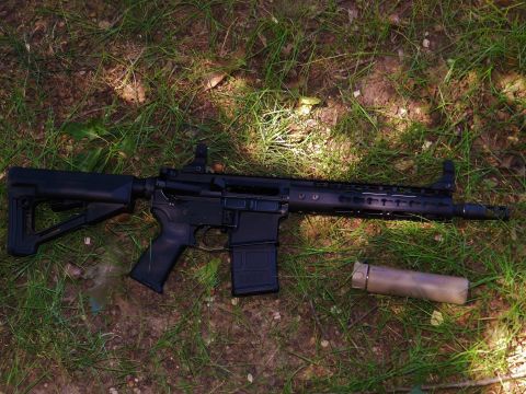 1996 Ford Bronco - An AR-15 style rifle and a suppressor are placed on the ground amidst grass and dirt.