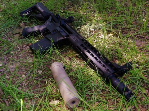 1996 Ford Bronco - An assault rifle with a suppressor rests on the grass, its tactical design evident.
