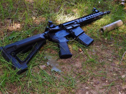 1996 Ford Bronco - Assault rifle with suppressor and magazine on the ground in grass.