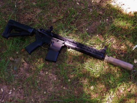 1996 Ford Bronco - A firearm with a silencer is placed on the ground amidst grass and soil.