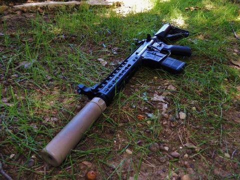 1996 Ford Bronco - Assault rifle with suppressor resting on the ground outdoors.