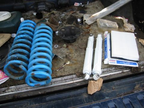 1985 Ford Bronco - Various vehicle suspension parts are laid out in the cargo area of a vehicle.