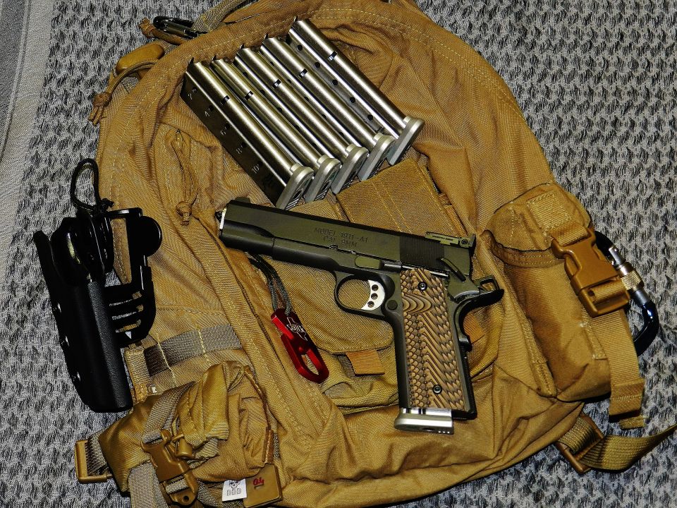 Pistol with textured grips and several magazines resting on a tan tactical backpack
