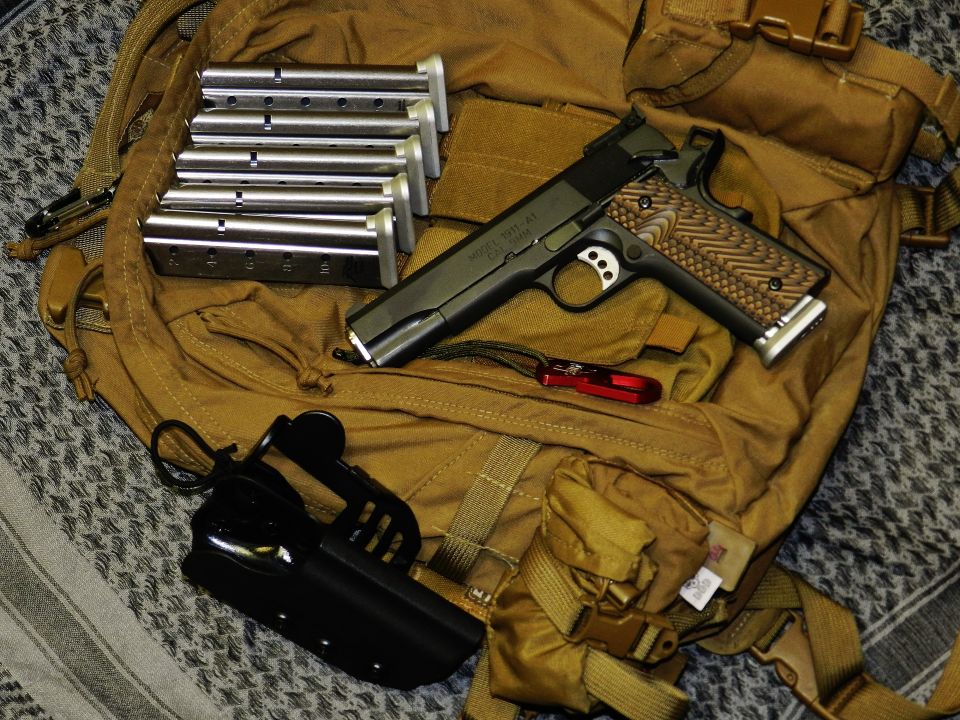 Pistol with five magazines, holster, and a multi-tool on a tan backpack
