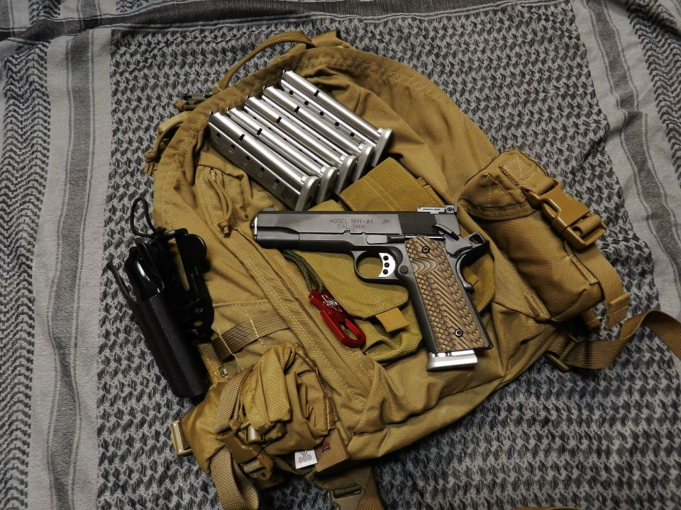 Tan backpack with a pistol, five magazines, and a black holster on a patterned cloth