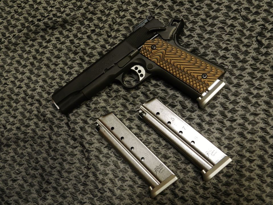 Black semi-automatic pistol with textured brown grips and two metal magazines on a patterned cloth