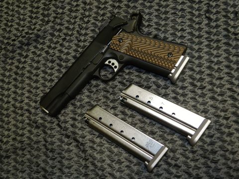 1996 Ford Bronco - A pistol with a textured grip and two magazines are displayed on a patterned surface. The image includes a watermark for Supermotors.net.