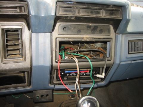 1985 Ford Bronco - The dashboard of a vehicle shows exposed wiring where the radio used to be, with visible air vents and controls.