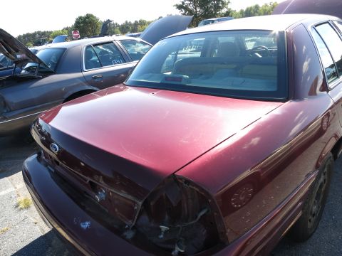 2001 Ford Crown Victoria - Rear view of a maroon 2001 Ford Crown Victoria at a junkyard, with another car visible to the left.