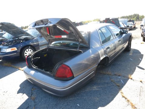 2001 Ford Crown Victoria - Two Ford Crown Victorias are parked in a lot, one with its trunk and hood open, the other missing rear wheels.