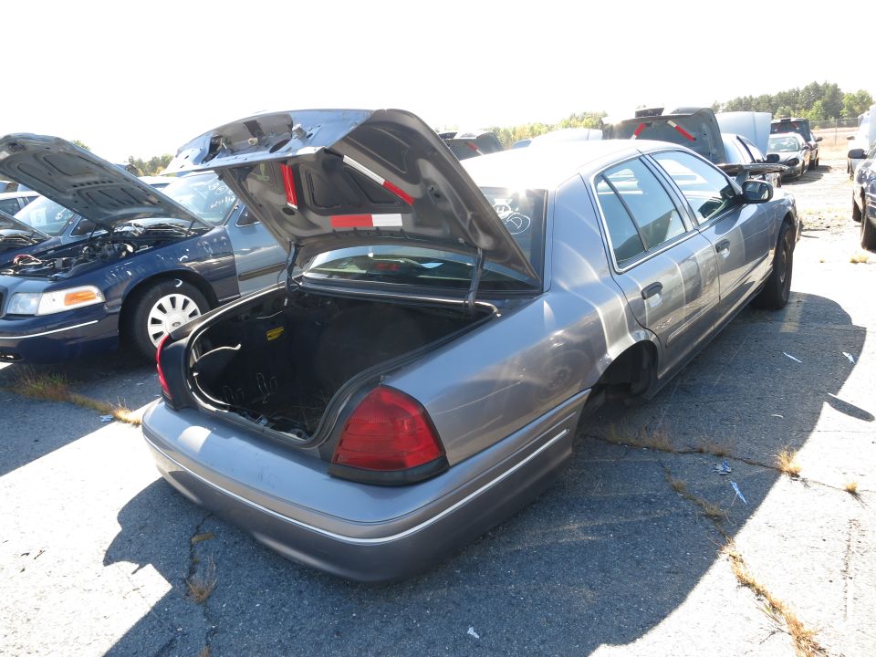 Gray Ford Crown Victoria with trunk open, missing rear wheels. Another Crown Victoria with hood open is next to it