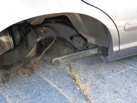 2001 Ford Crown Victoria - The rear suspension of a silver car is visible, showing a missing wheel and a damaged lower control arm.