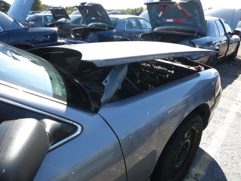 2001 Ford Crown Victoria - A light blue 2001 Ford Crown Victoria sits in a junkyard with its hood open, revealing the engine compartment.
