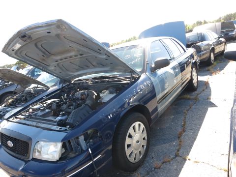 2001 Ford Crown Victoria - Blue 2001 Ford Crown Victoria in a junkyard with its hood open, revealing the engine.