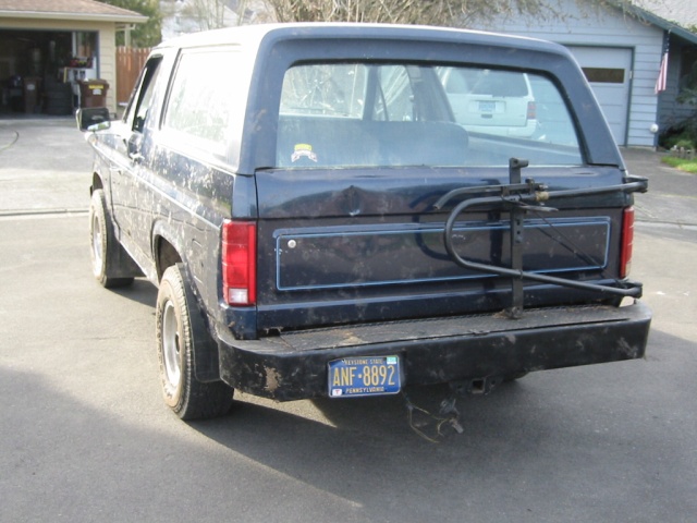 Dark blue SUV, rear view, with a bike rack and license plate ANF-8892. Dented tailgate