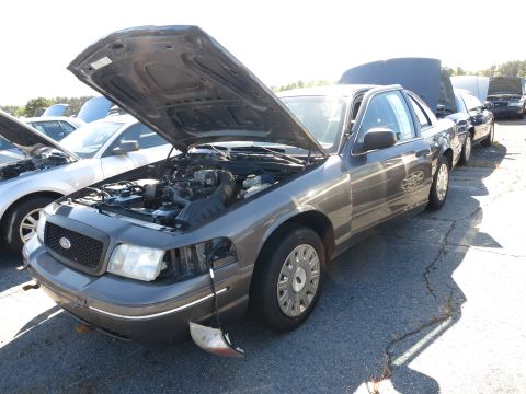 2001 Ford Crown Victoria - A dark gray Ford Crown Victoria sits with its hood open, parked in a lot with other vehicles.