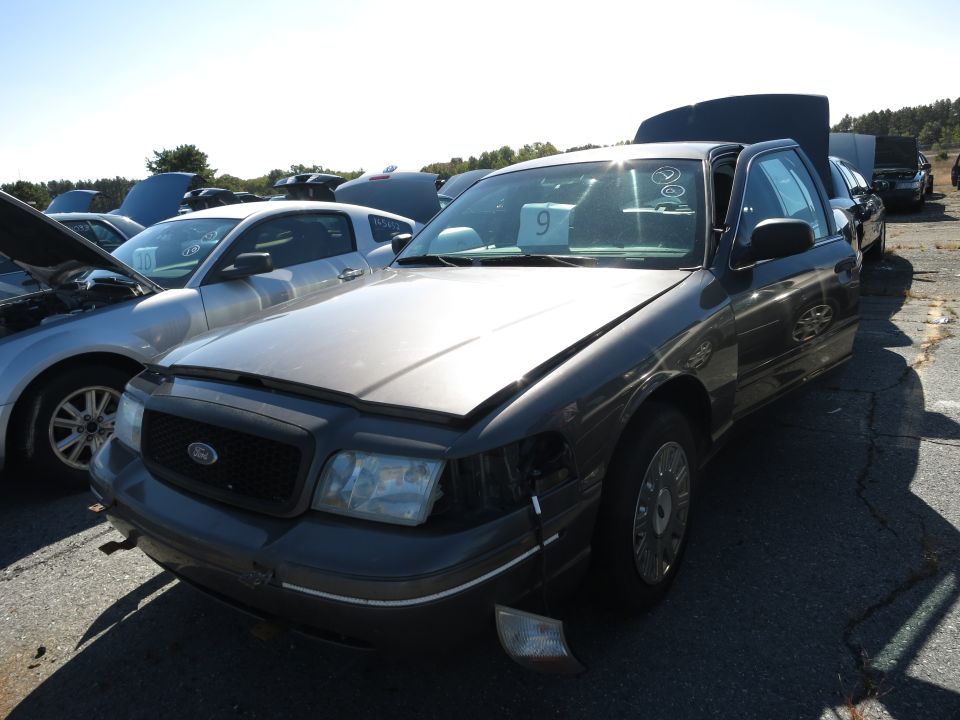 Dark gray 2001 Ford Crown Victoria with a damaged front bumper and missing headlight, parked in a lot with other vehicles