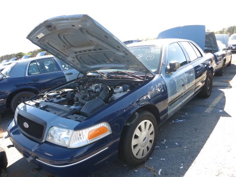 2001 Ford Crown Victoria - A blue and light blue 2001 Ford Crown Victoria is parked with its hood open, revealing the engine compartment. Another similar vehicle is v…