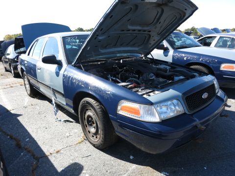 2001 Ford Crown Victoria - Two Ford Crown Victorias are parked outside, one with its hood open revealing the engine.
