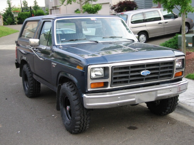 Dark blue lifted Ford Bronco SUV with off-road tires, front three-quarter view on suburban street
