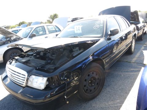 2001 Ford Crown Victoria - A black Ford Crown Victoria sits in a lot with its hood open, alongside other vehicles.