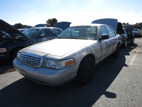 2001 Ford Crown Victoria - Several cars are parked in an outdoor lot, some with their hoods open under a clear sky.