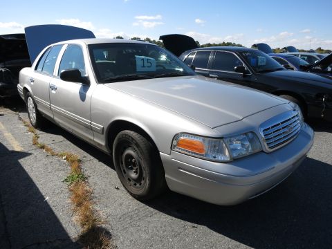 2001 Ford Crown Victoria - A silver sedan is parked in a lot with other vehicles, some with hoods open.