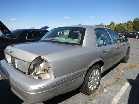 2001 Ford Crown Victoria - A silver 2001 Ford Crown Victoria is parked outdoors, showing damage to its rear with a missing taillight assembly.
