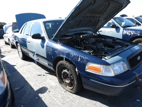2001 Ford Crown Victoria - A damaged police car sits in a lot with its hood open, revealing the engine compartment. Text on the fender reads 'STATE POLICE'.