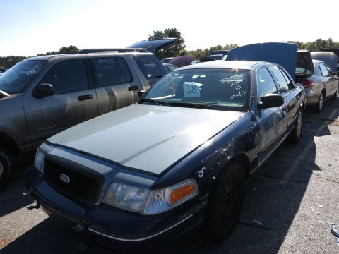2001 Ford Crown Victoria - A dark blue Ford Crown Victoria with a gray hood sits in a lot with other vehicles under a clear sky.