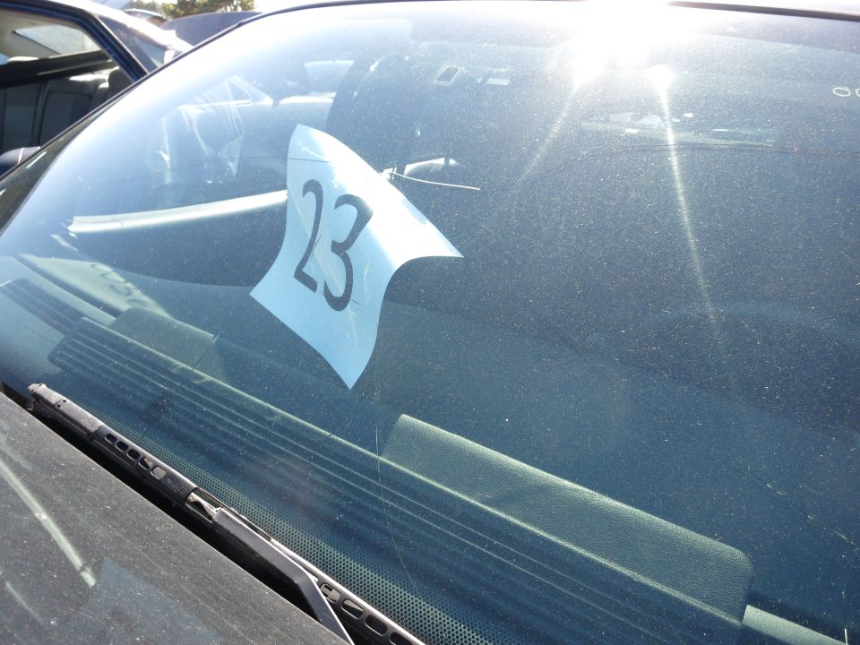 Windshield with blue paper displaying number 23, sun glare, and part of a dashboard