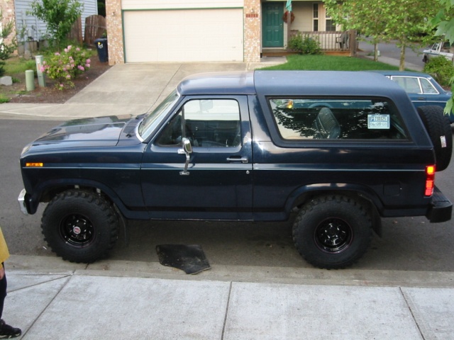 Dark blue Ford Bronco SUV in side profile with black steel wheels and off-road tires, parked in a driveway