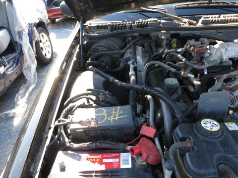 2001 Ford Crown Victoria - The engine compartment of a vehicle, showing the battery and electrical components, with other vehicles in the background.