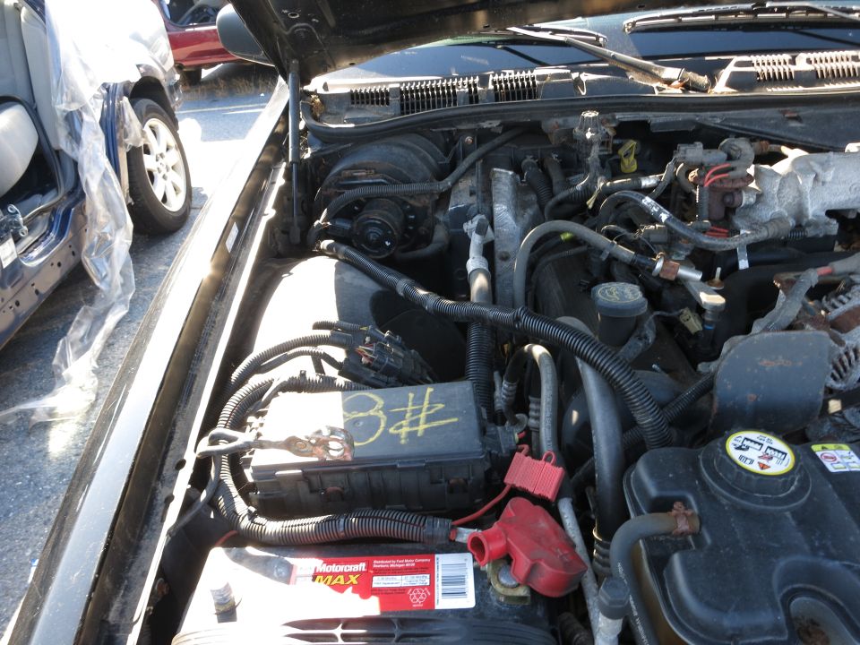 Engine bay with battery, fuse box labeled 'B#', and various hoses and wiring. Another vehicle is partially visible to the left