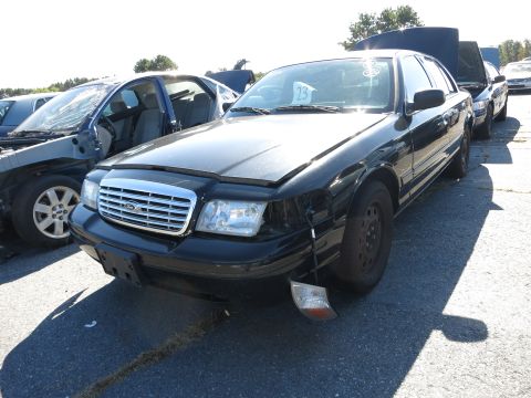 2001 Ford Crown Victoria - A black 2001 Ford Crown Victoria sits in a junkyard with other vehicles.