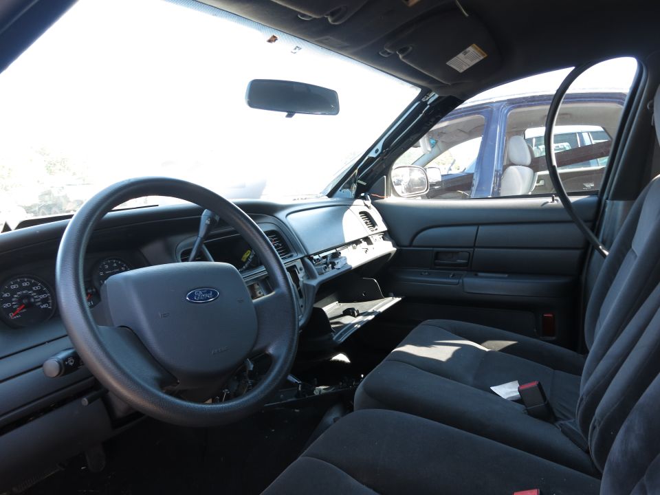 Interior view of a 2001 Ford Crown Victoria showing the dashboard, steering wheel, and seats. Another vehicle is visible through the window