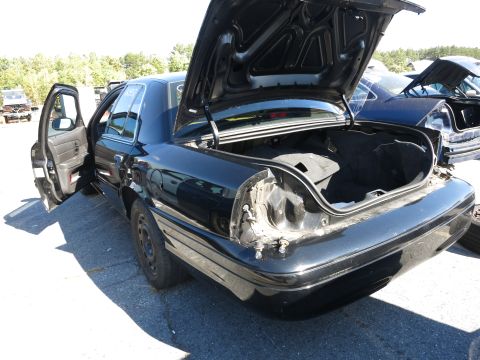 2001 Ford Crown Victoria - A black 2001 Ford Crown Victoria sits in a junkyard with its trunk and driver's door open, revealing damage to the rear.