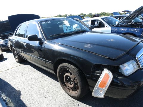 2001 Ford Crown Victoria - A black sedan sits in a lot with other vehicles, one of which has a '23' sign on its windshield.